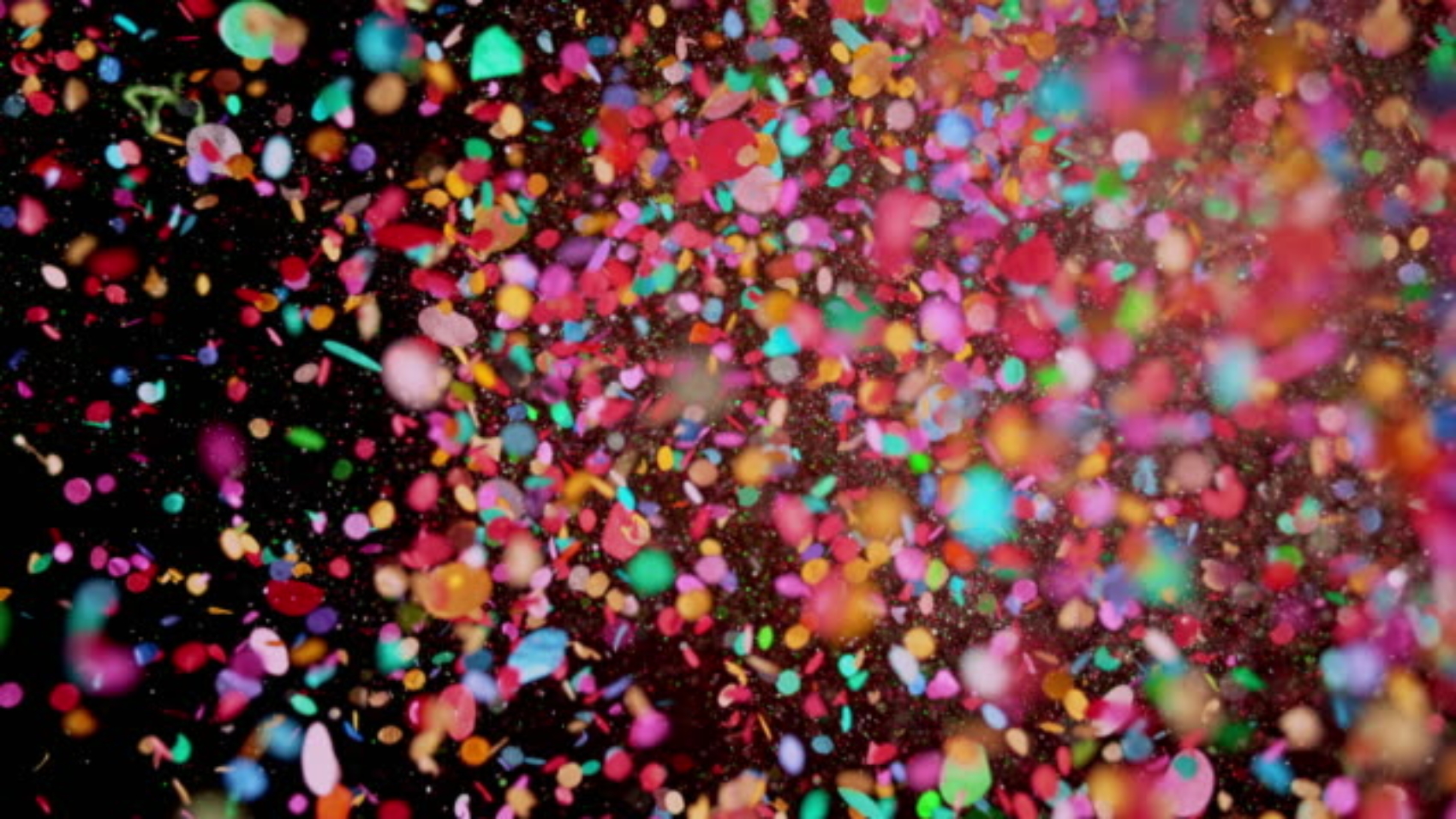 Slow motion close up locked down shot of colorful confetti flying towards the camera against black background. Shot in Slovenia.